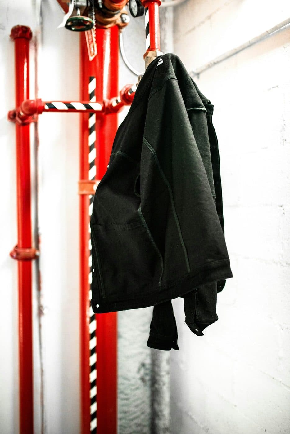 Black jacket hanging on a red clothes rack against a white wall