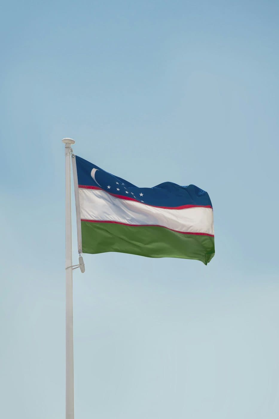 Uzbekistan flag flying against a pale sky