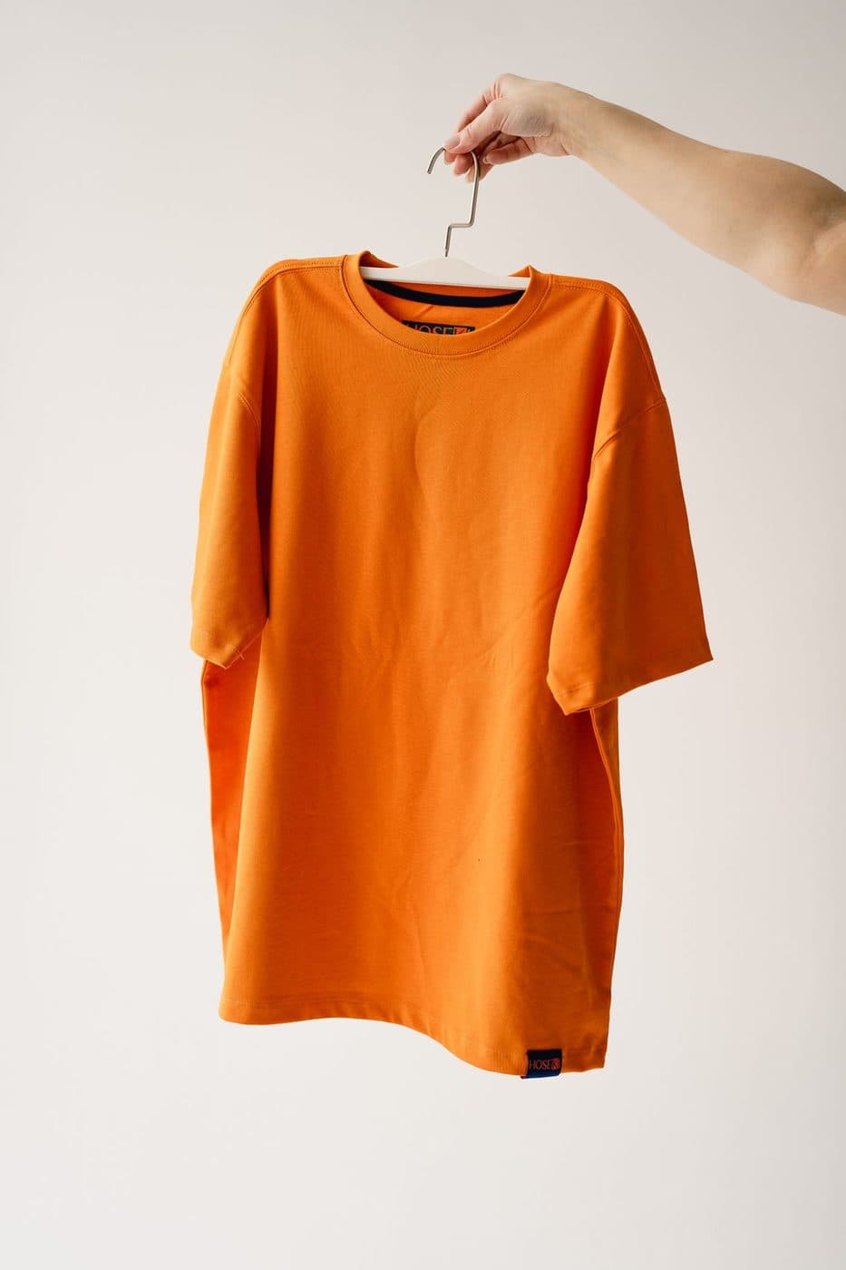 Orange crew-neck t-shirt on a hanger against a white wall