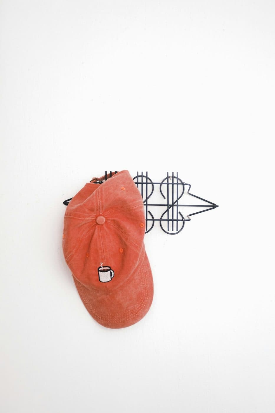 Orange baseball cap hanging on a white wall